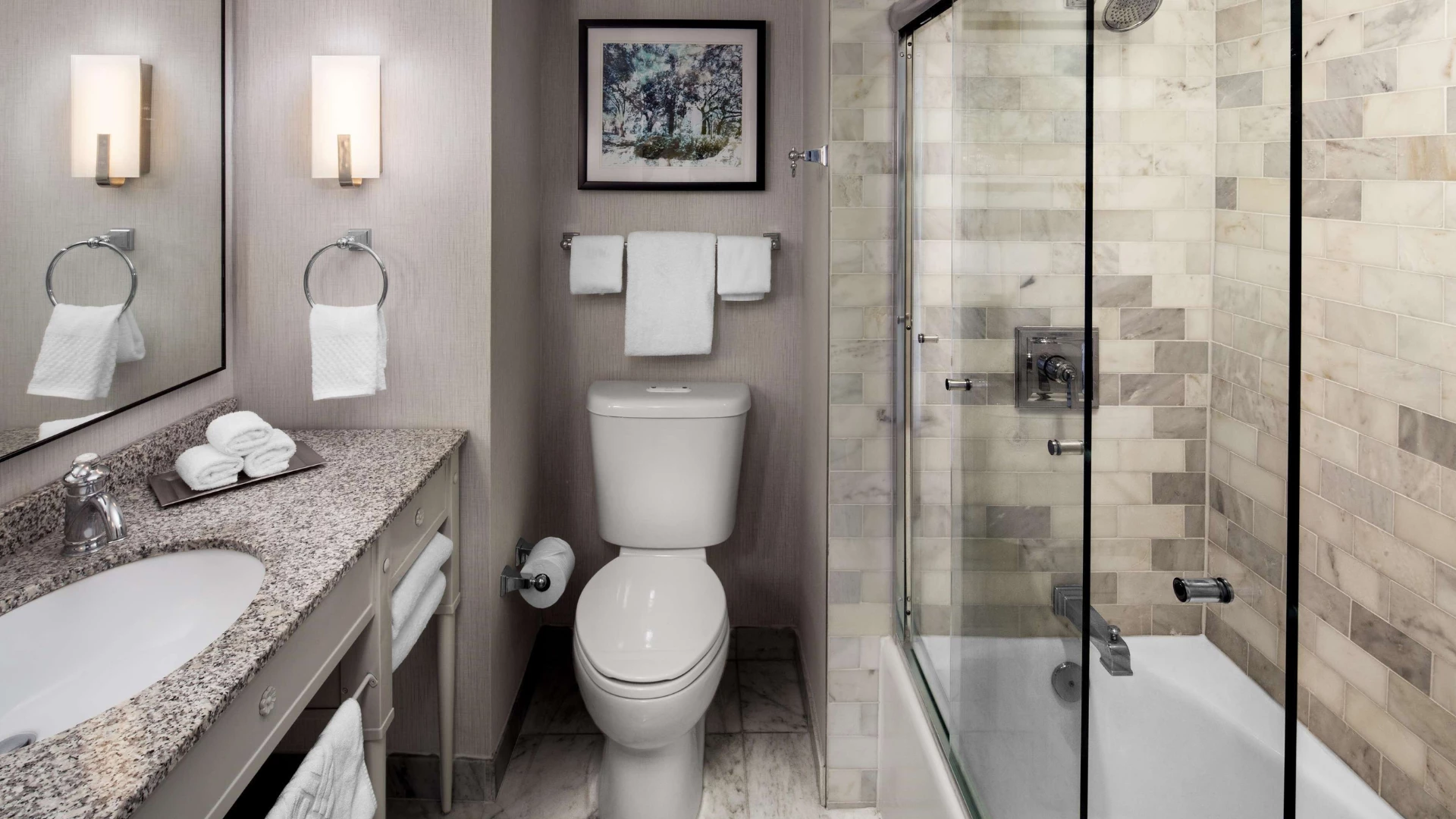 A clean and modern bathroom with a granite countertop, glass-enclosed shower, and a toilet.