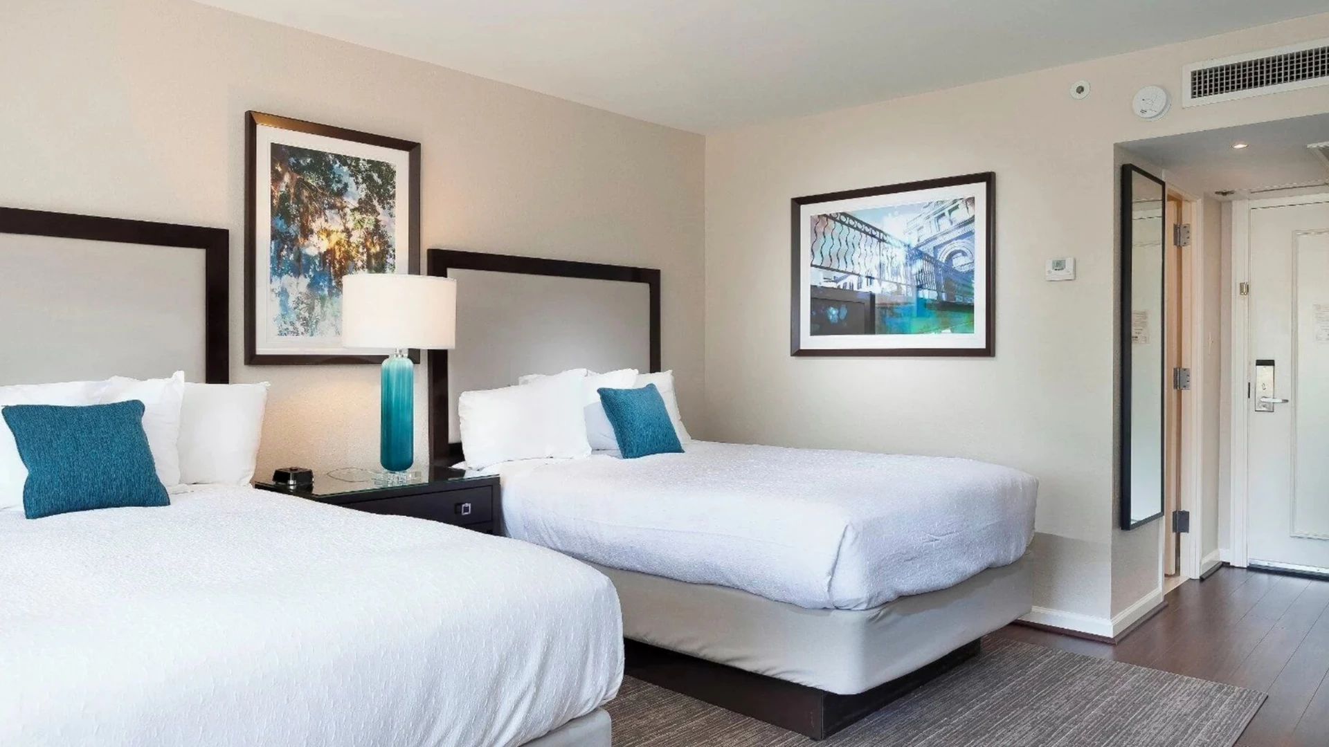 A hotel room with two beds, a nightstand, and artwork on the walls