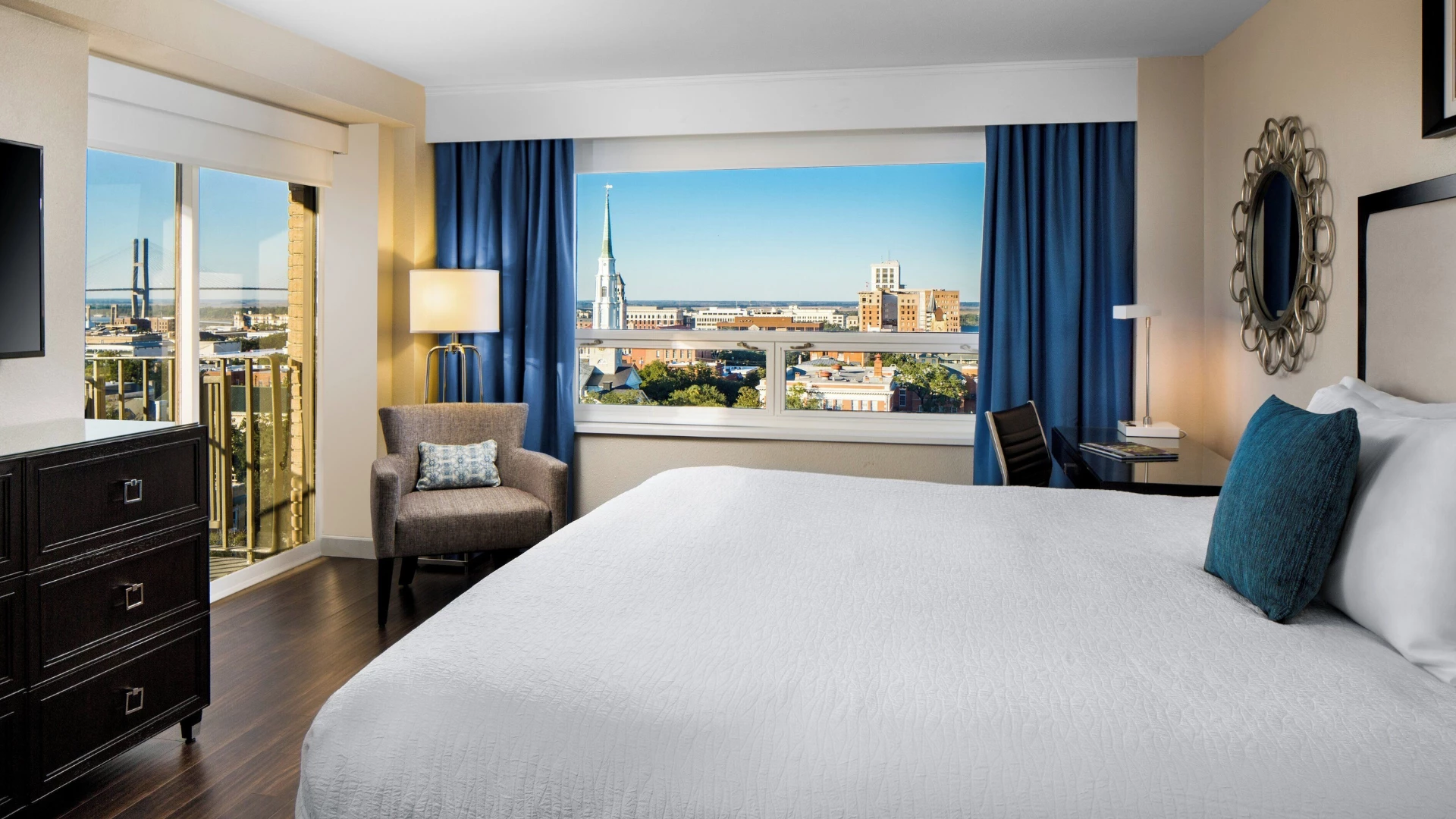 A hotel room with a large bed, balcony, and city view.