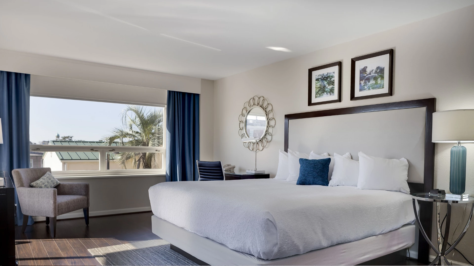 A hotel room with a large bed, chair, desk, and window with a view.