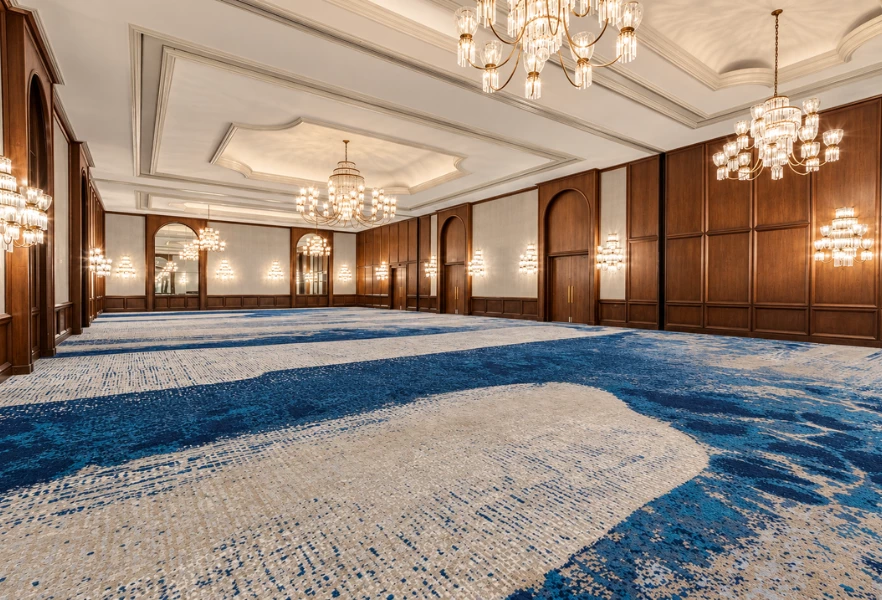 A large, empty meeting room with blue and white carpet, wood paneling, and chandeliers.