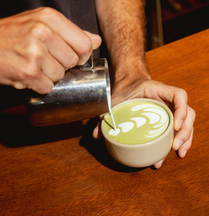 a person pouring milk into a cup of green latte