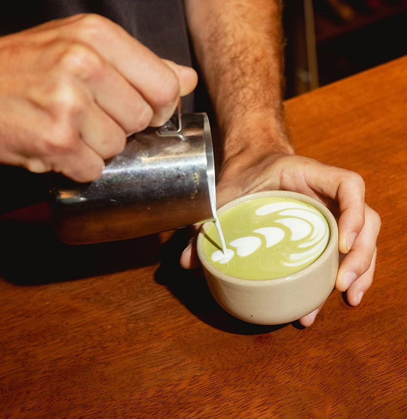 a person pouring milk into a cup of green latte