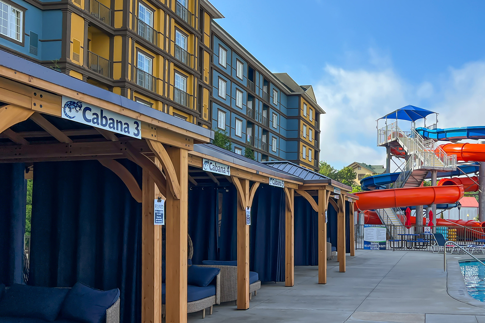 A row of cabanas by the pool with a water slide in the background