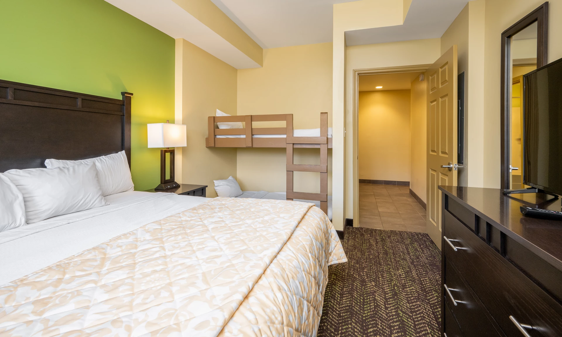A hotel room with a queen bed, bunk bed, dresser, and TV