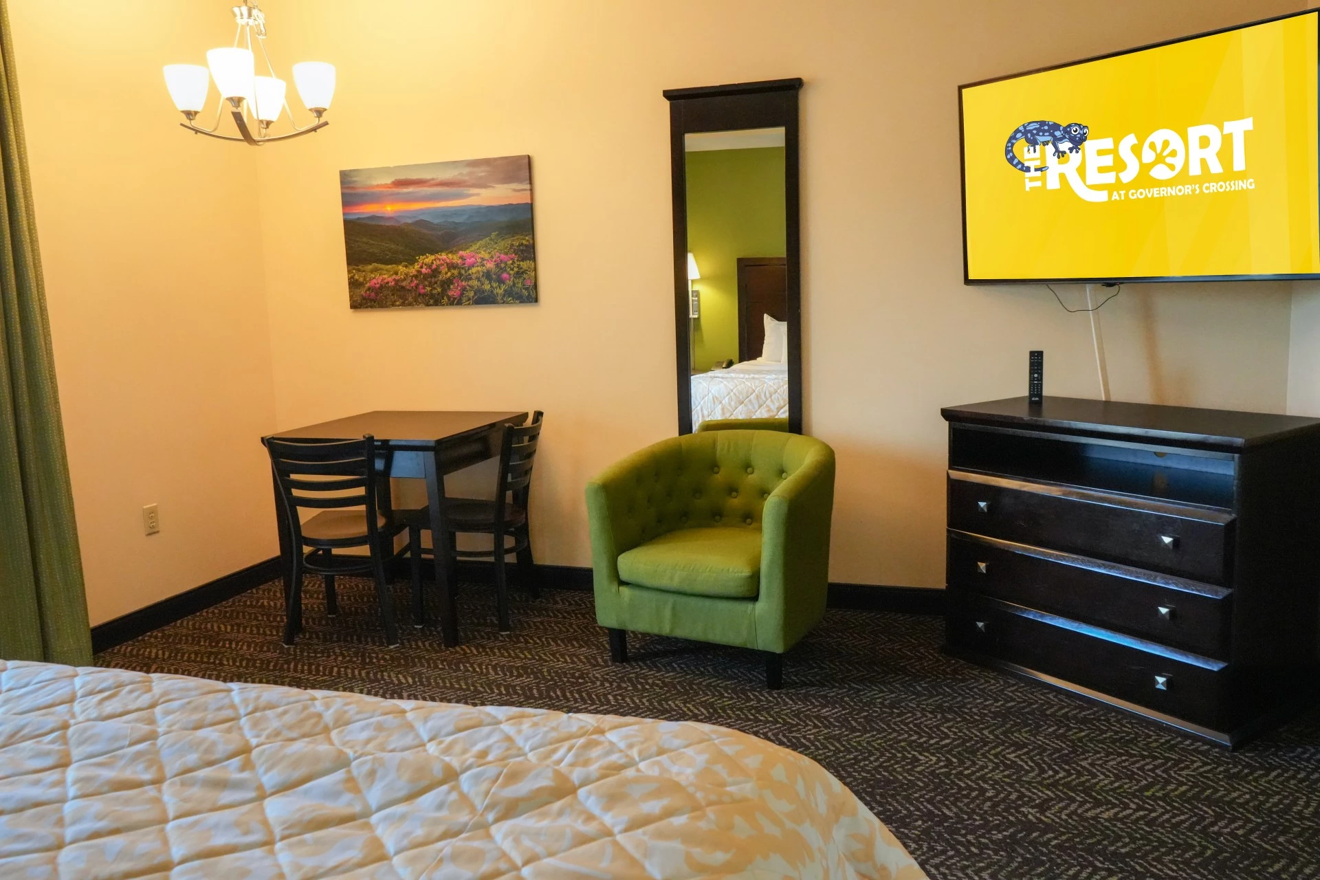 A hotel room with a bed, TV, dresser, chair, and table.