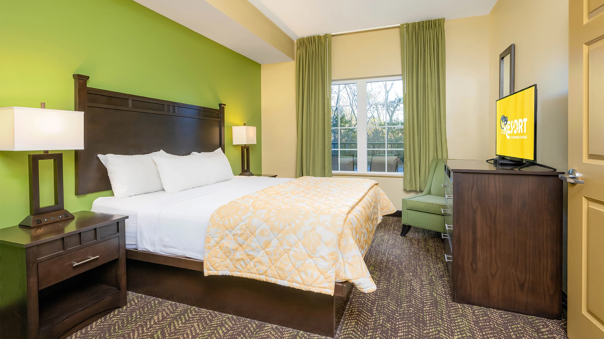 A hotel room with a bed, TV, window, chair, and lamps