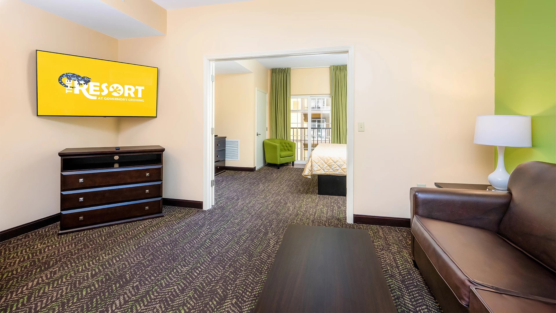 A hotel room with a living area, bedroom in the background, and balcony access.