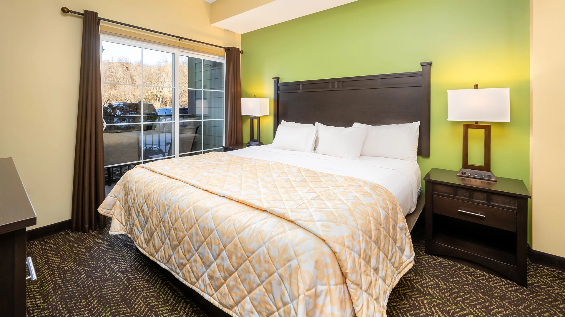 A wide-angle view of a hotel room with a large bed, two nightstands, and a window