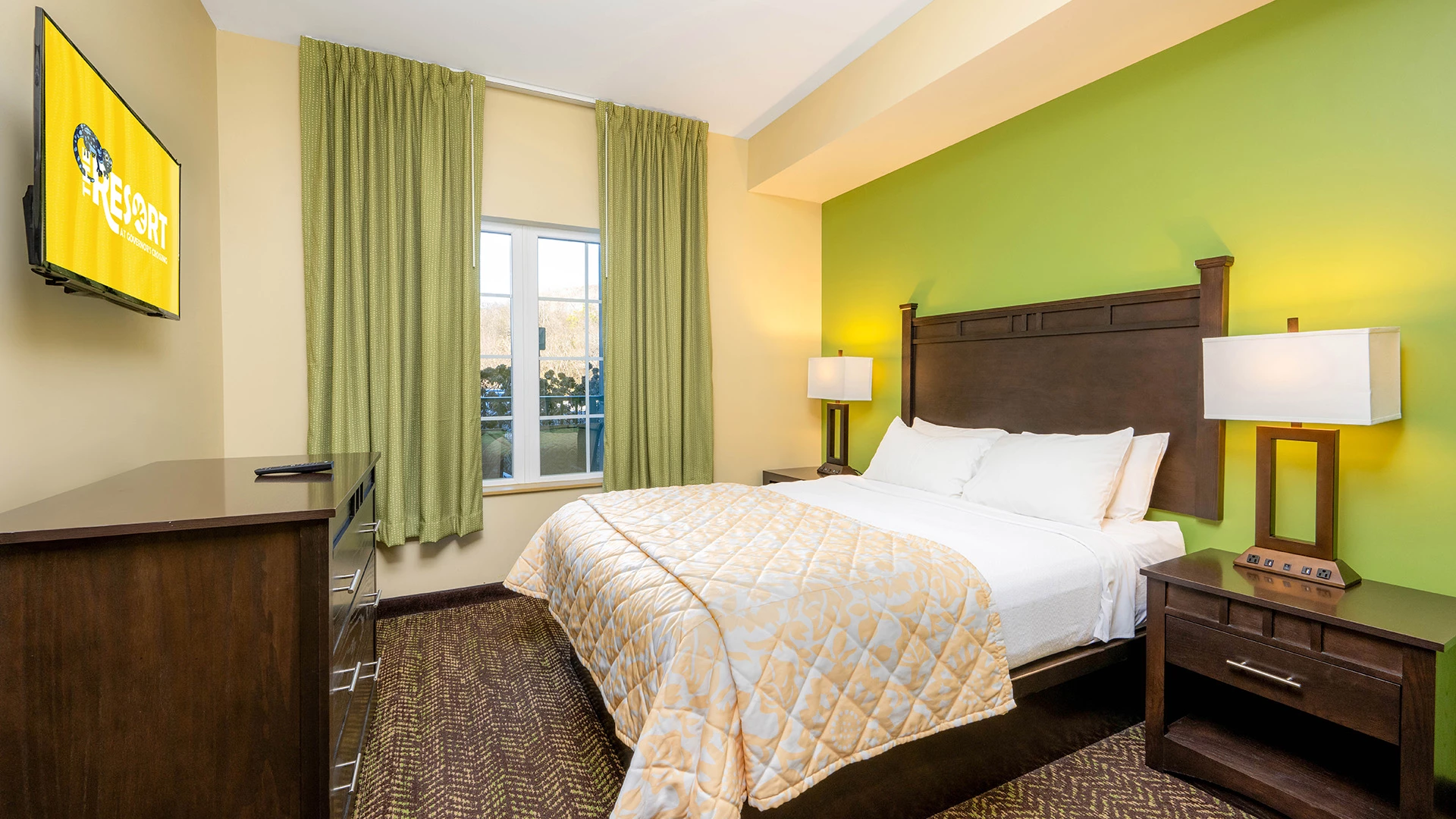 A hotel room with a bed, TV, dresser, and nightstand.