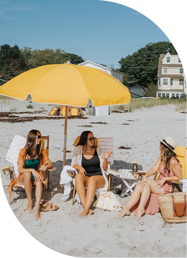 a group of women sitting under a yellow umbrella on a beach