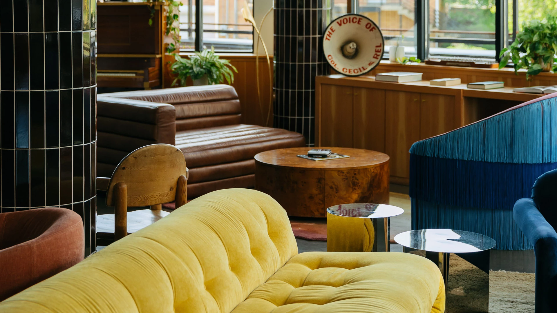A stylish lobby seating area with a yellow couch, brown leather seating, and a blue fringed chair.