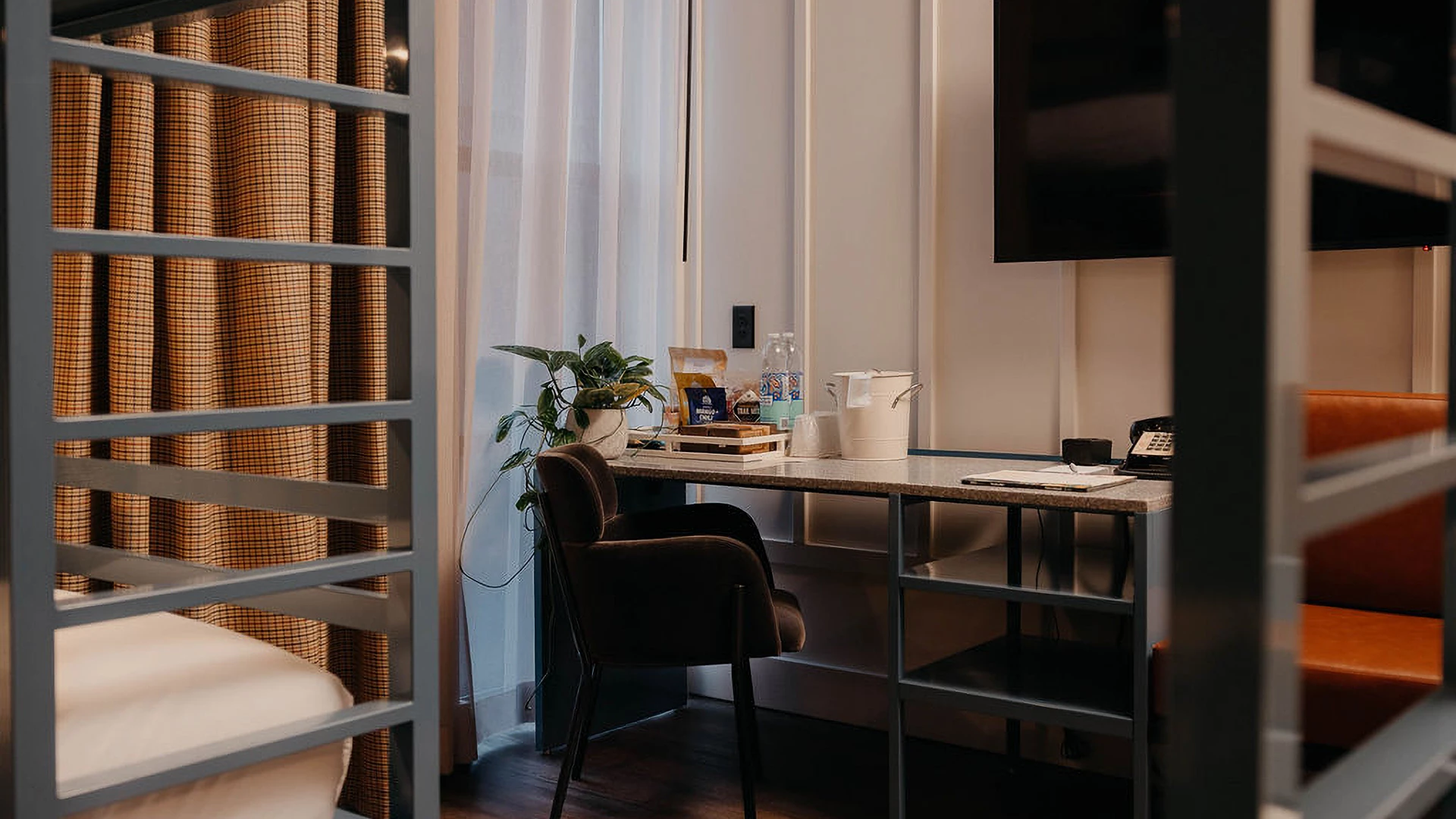 A hotel room with a desk, chair, TV, and bunk beds.