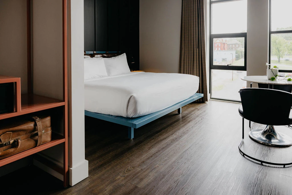 A hotel room with a blue bed frame, white bedding, and a large window