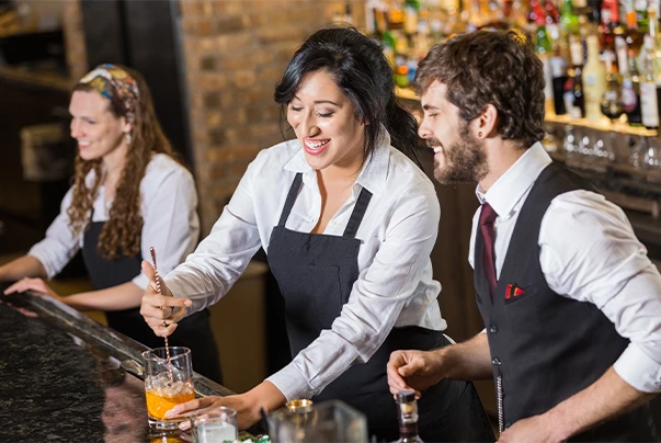 Three people behind a bar preparing drinks