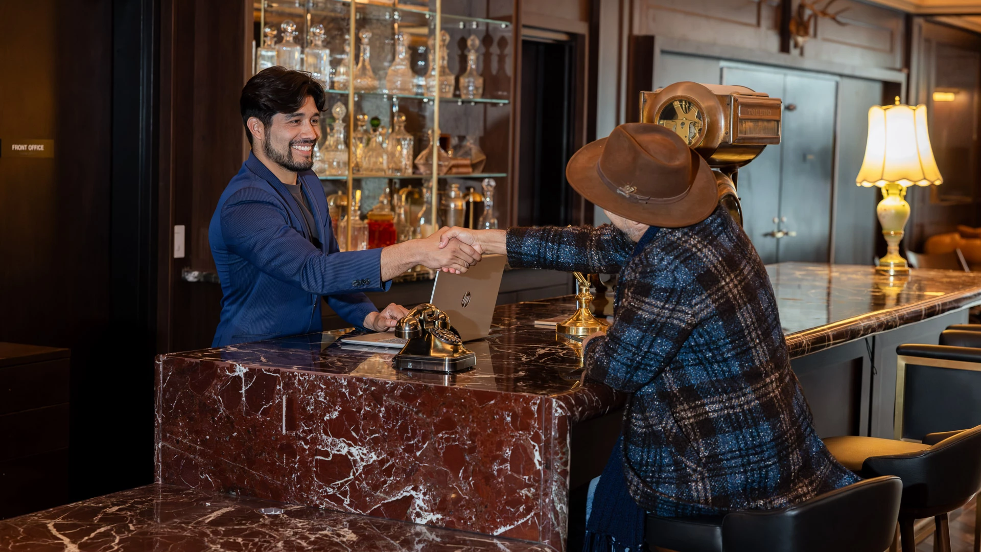 Two men shaking hands behind a marble bar in a lobby.