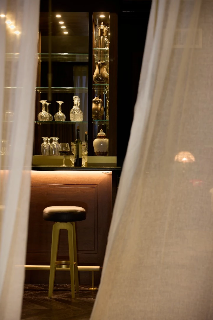 a bar with a stool, shelves of bottles and glasses, and curtains