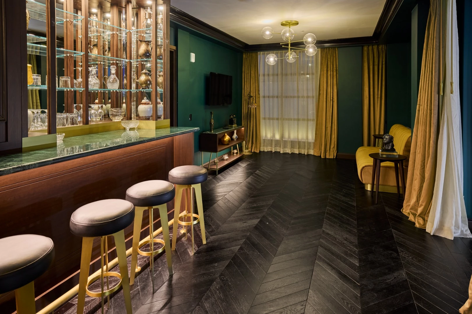 A luxurious bar with a green counter, wooden shelves, and four stools.
