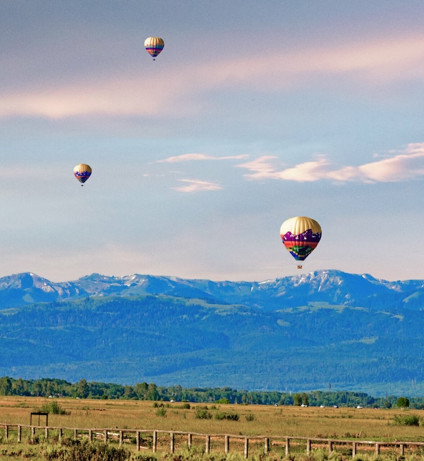three hot air balloons at various levels of height in the sky over a field
