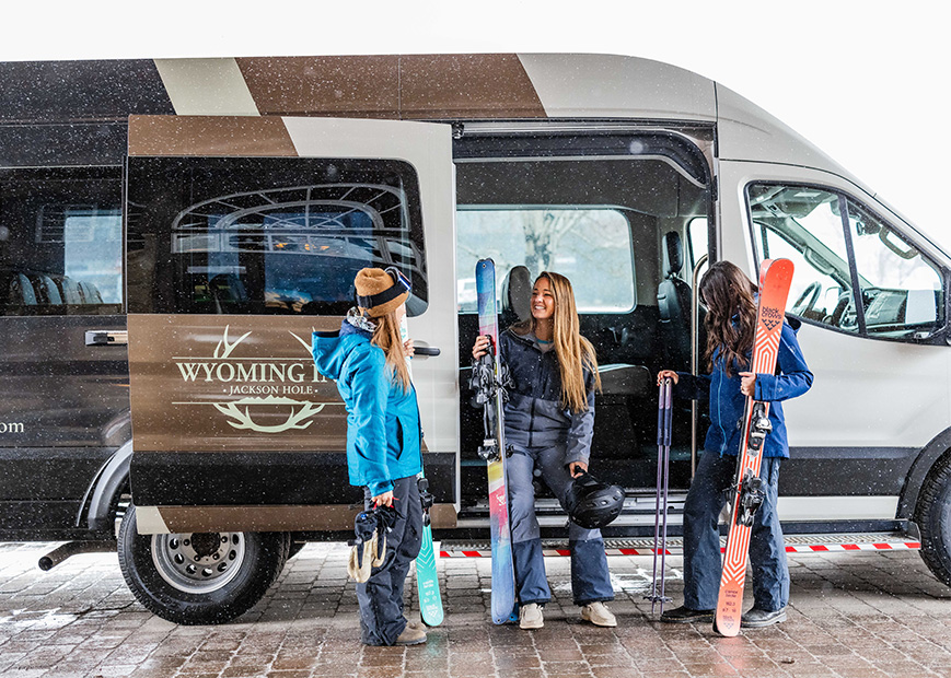 a group of women with skis and snowboards standing in front of a van