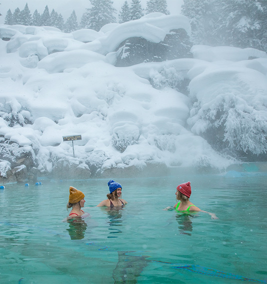 a group of women in a pool of water with snow covered mountains