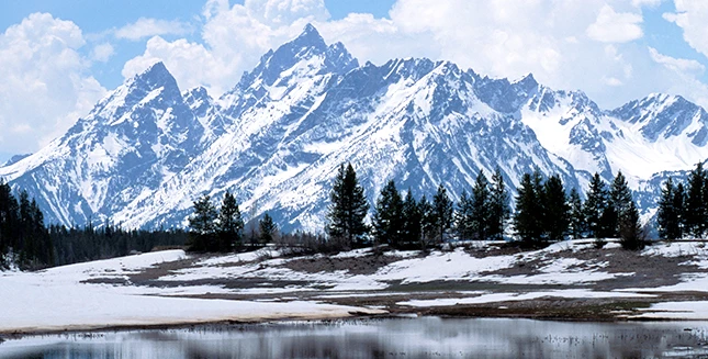 a snowy mountain range with trees and a lake