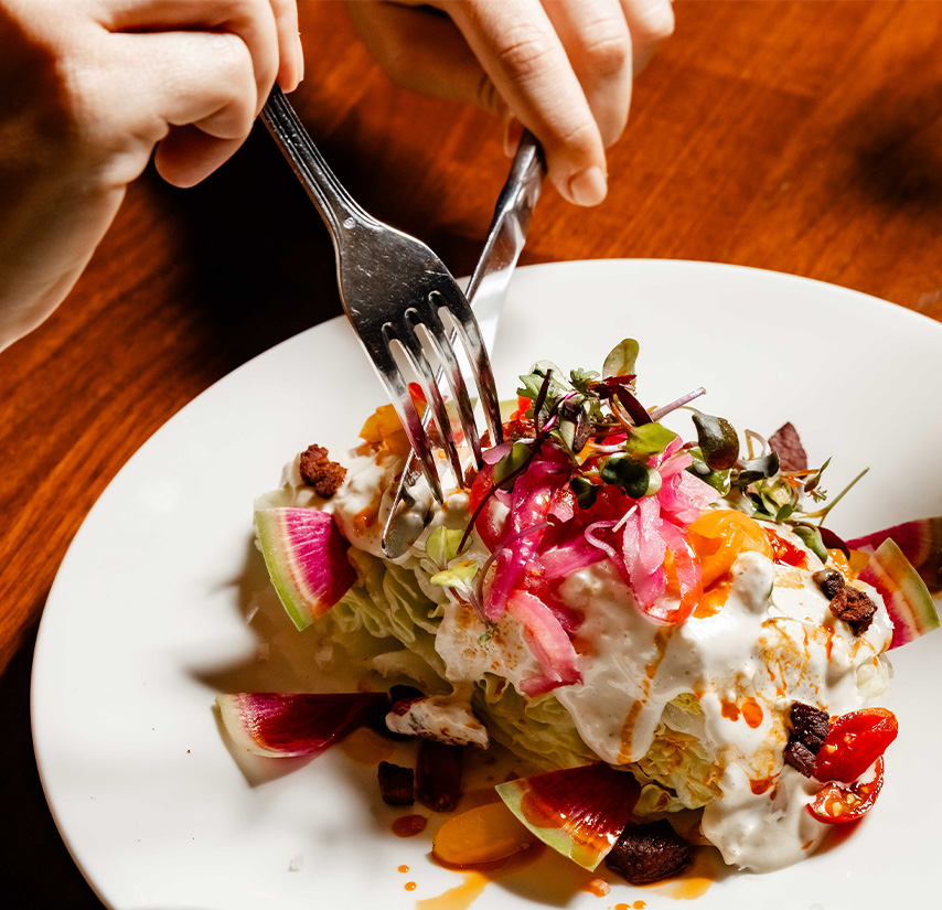 a person holding a fork and knife to a plate of food