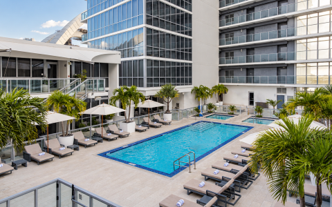 a pool with lounge chairs and umbrellas in front of a building