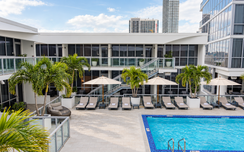 a pool with lounge chairs and umbrellas in front of a building