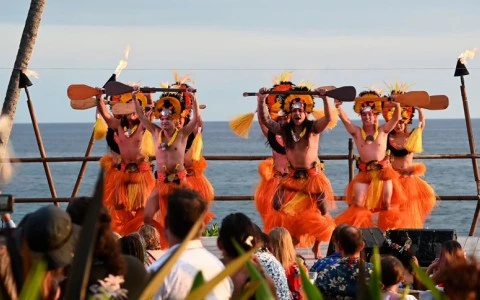 a group of men in clothing holding paddles and standing on stage at Luau at Royal Kona Resort