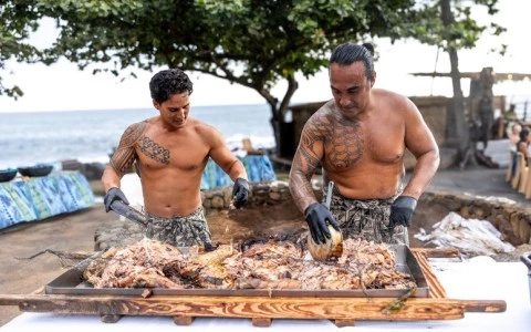 two men cooking meat on a large grillen shredding pork at luau at Royal Kona Resort