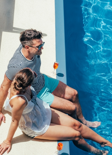 a man and woman sitting on a ledge near a pool