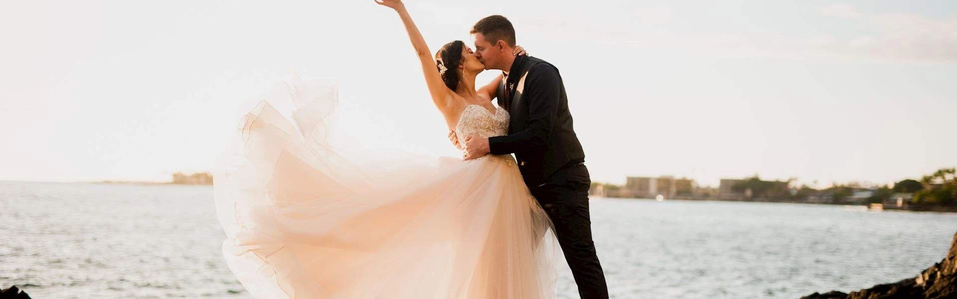 bride and groom kissing by the rocky beach