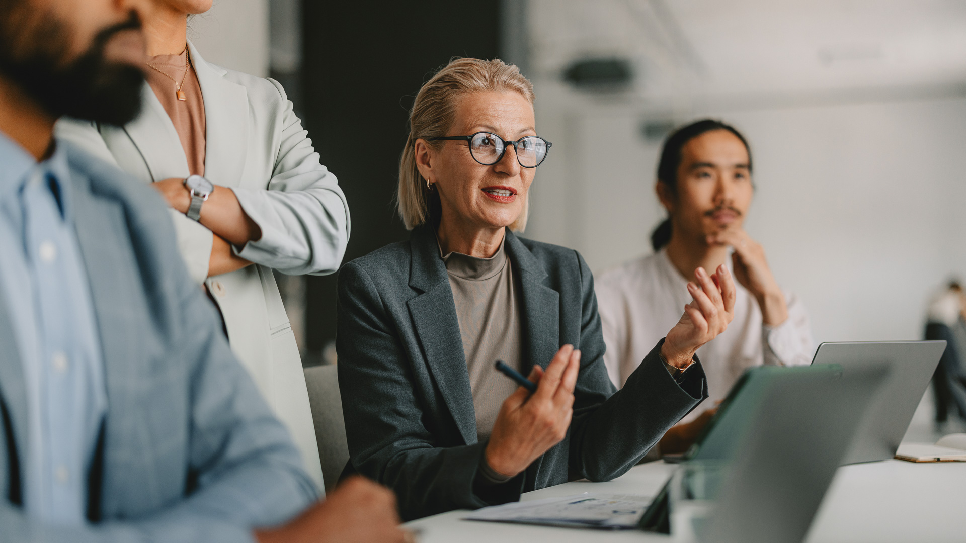 a woman in a suit and glasses sitting at a table with people in the background