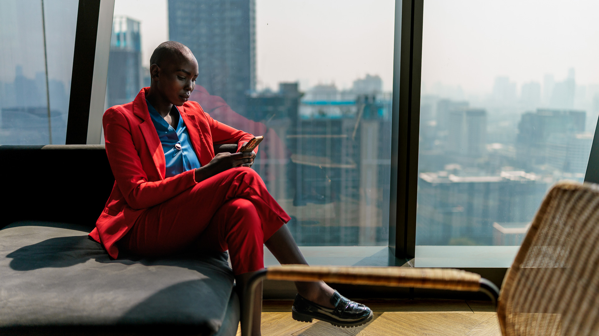 a woman in red suit sitting on a bench looking at her phone