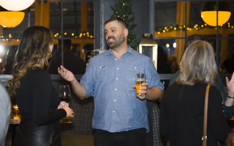 a man holding glasses of beer and talking to a group of people