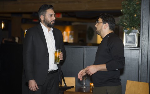 a man in a suit holding a glass of beer and talking to another man