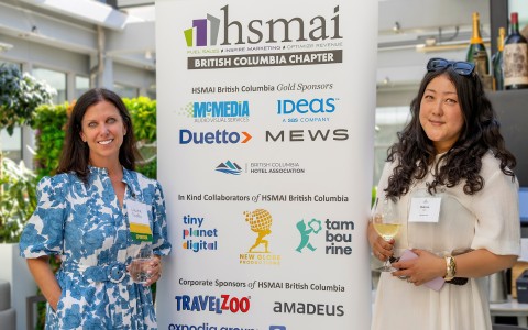 two women holding drinks and standing next to a sign
