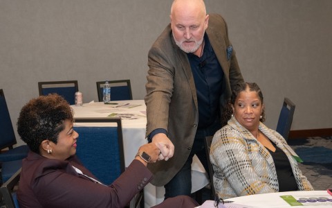 a man shaking hands with a woman sitting at a table
