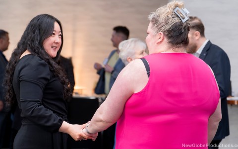 a woman in a pink dress shaking hands with another woman in a room
