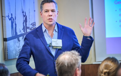 a man in a blue jacket speaking to a group of people