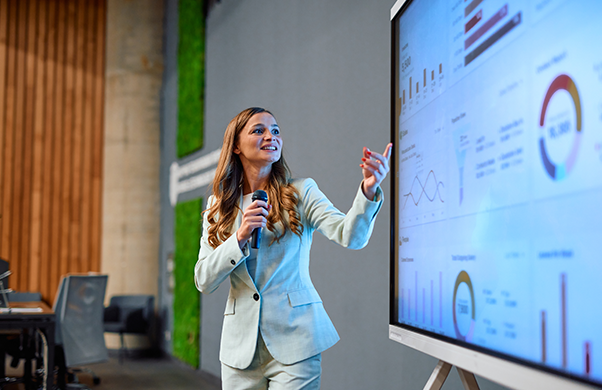 a woman in a suit pointing at a screen