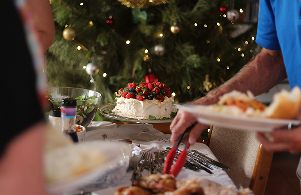 a person cutting a cake with a christmas tree in the background