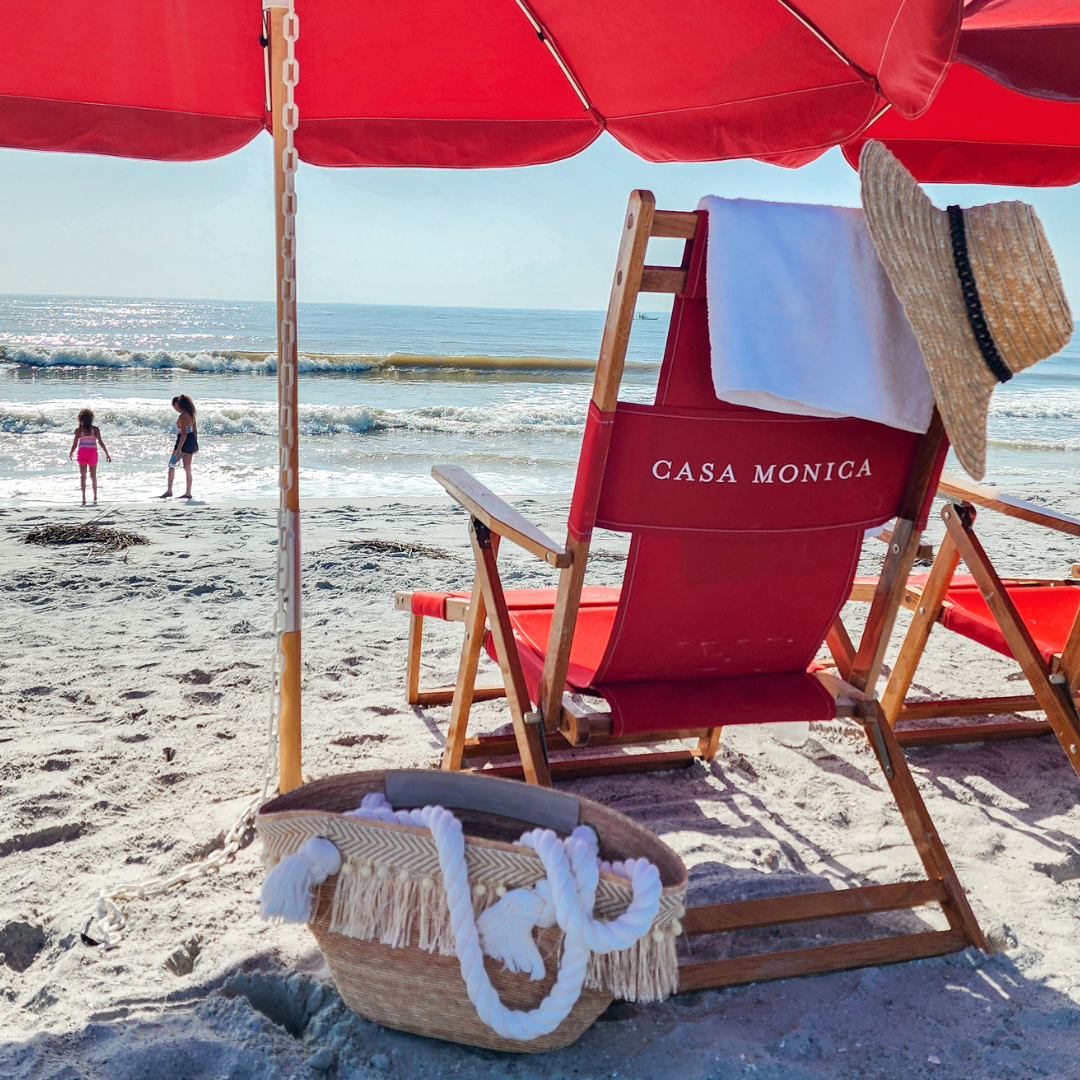 a beach chair with a straw hat and a basket on the beach