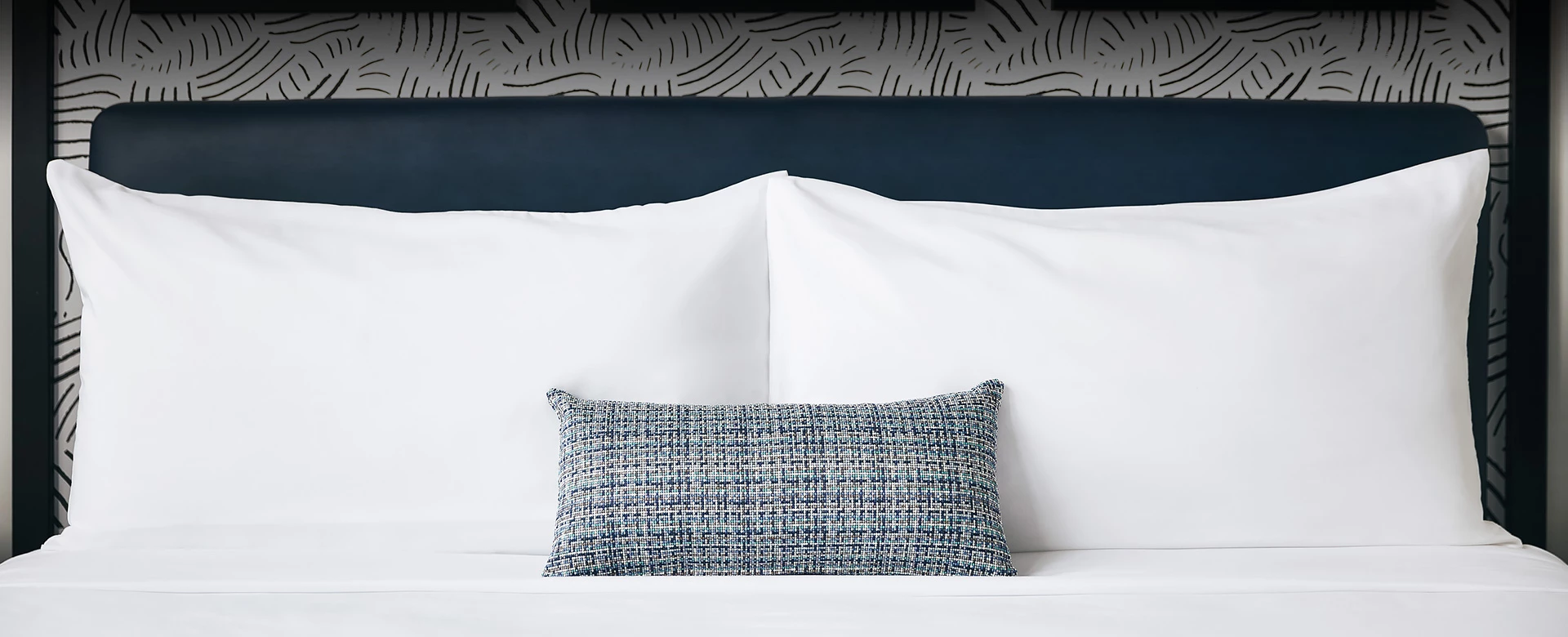 hotel room with white linens and one decorative gray pillow