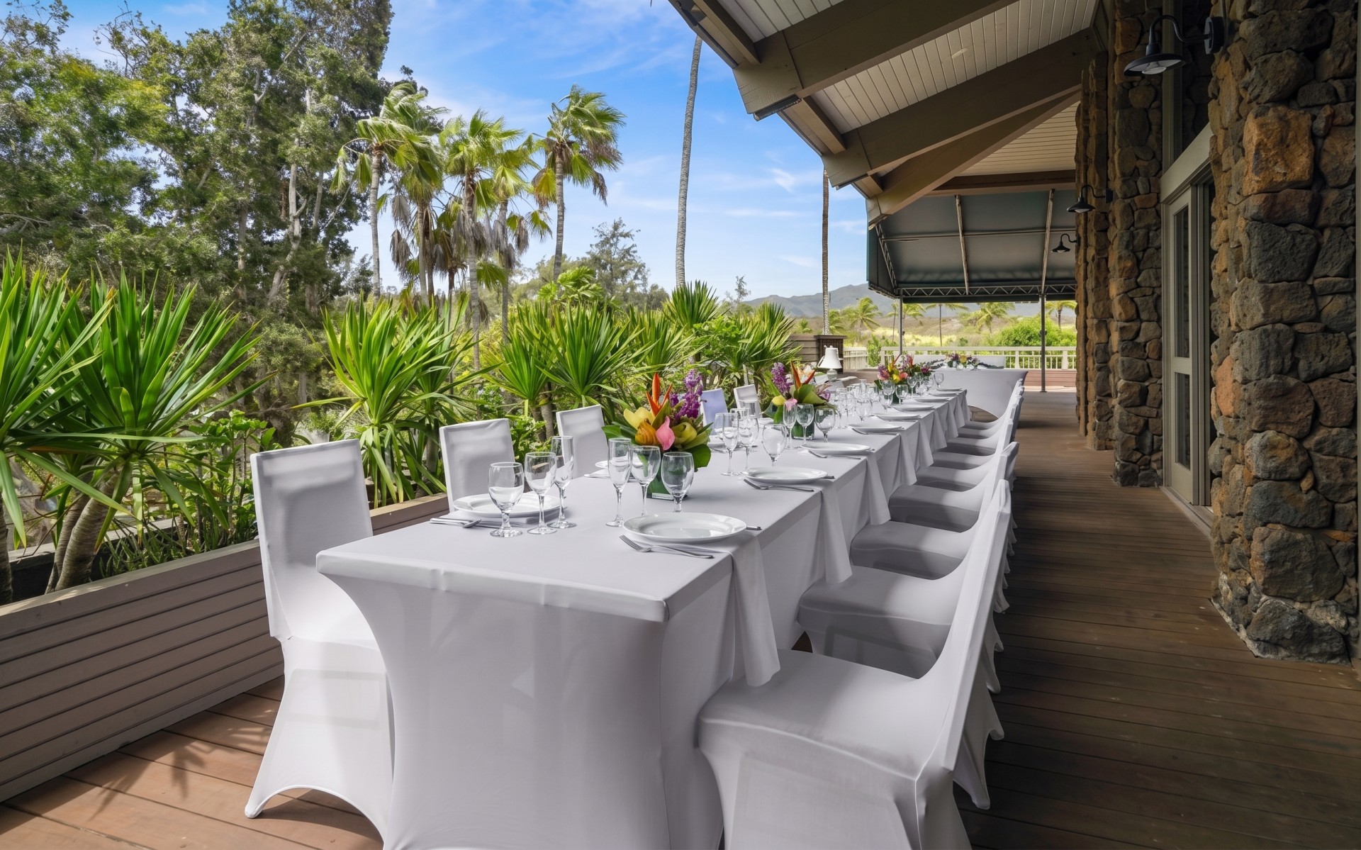 a long table set with white chairs and flowers on it