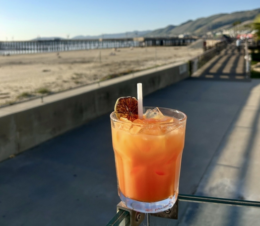 a glass of orange liquid with a straw and a slice of orange on a railing
