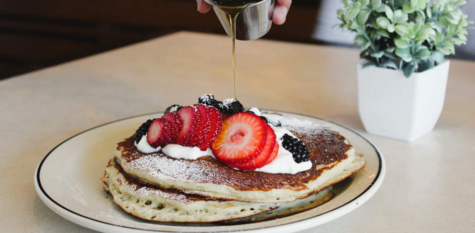 a person pouring syrup onto a stack of pancakes