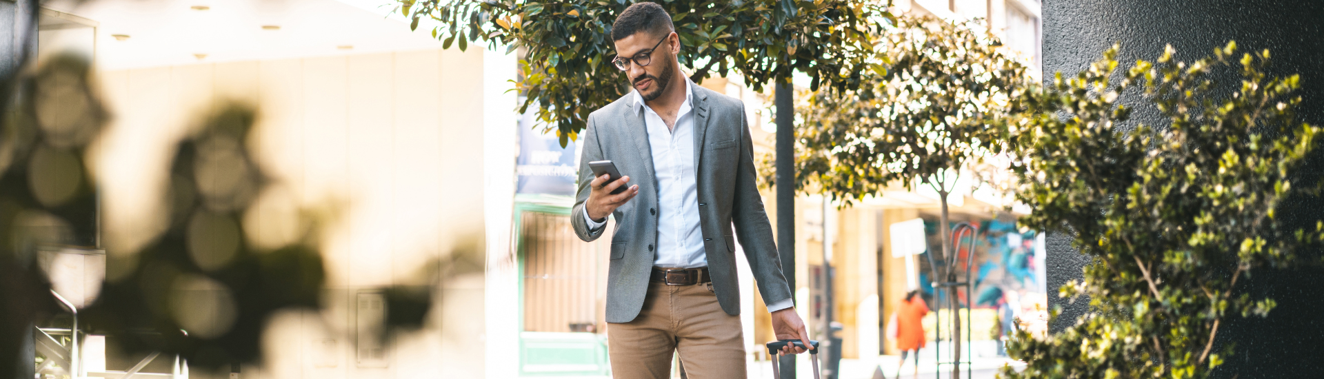 man in a suit wheeling a suitcase while looking at his phone