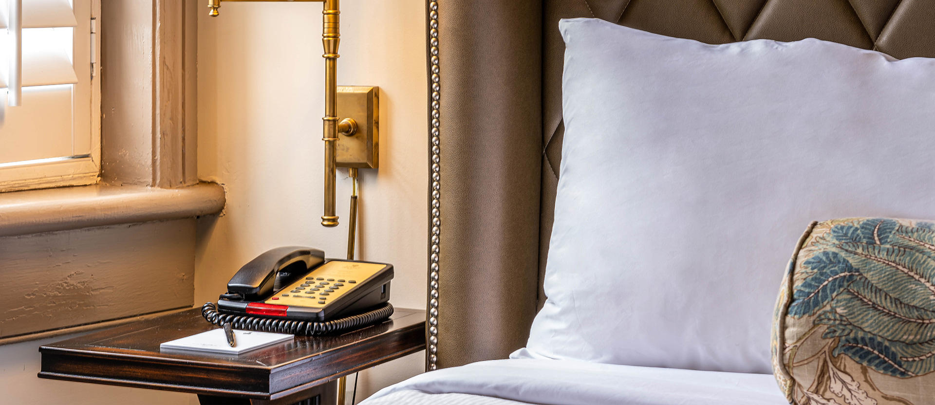 close up view to a. headboard, a pillow and a night table with a phone